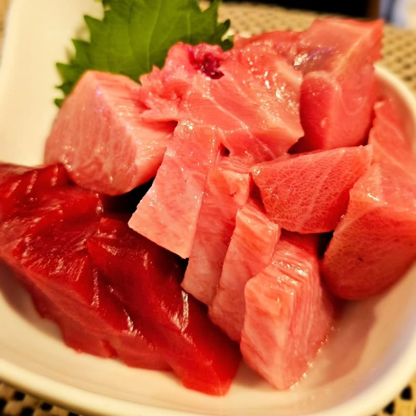 Close-up of a white plate filled with various cuts of fresh, raw tuna sashimi.